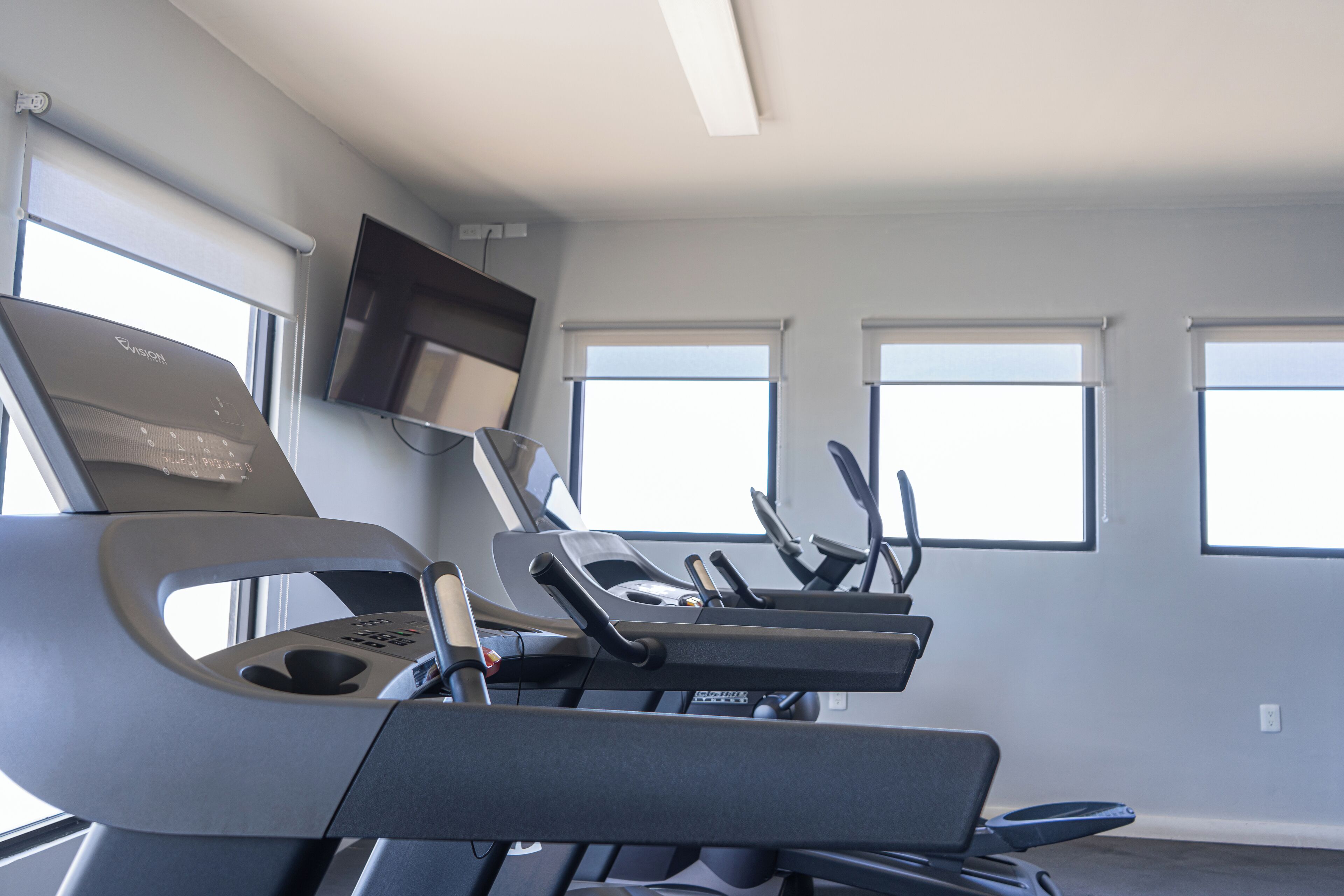 A gym with treadmills, a stationary bike, and a television mounted on the wall.