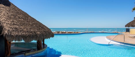 A swimming pool with a view of the ocean, surrounded by thatched-roof structures.