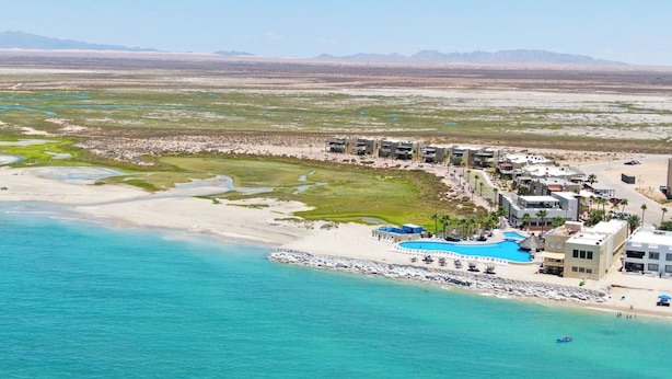 Vue aérienne d’une station balnéaire dotée d’une grande piscine, de villas en bord de mer et d’une plage de sable.