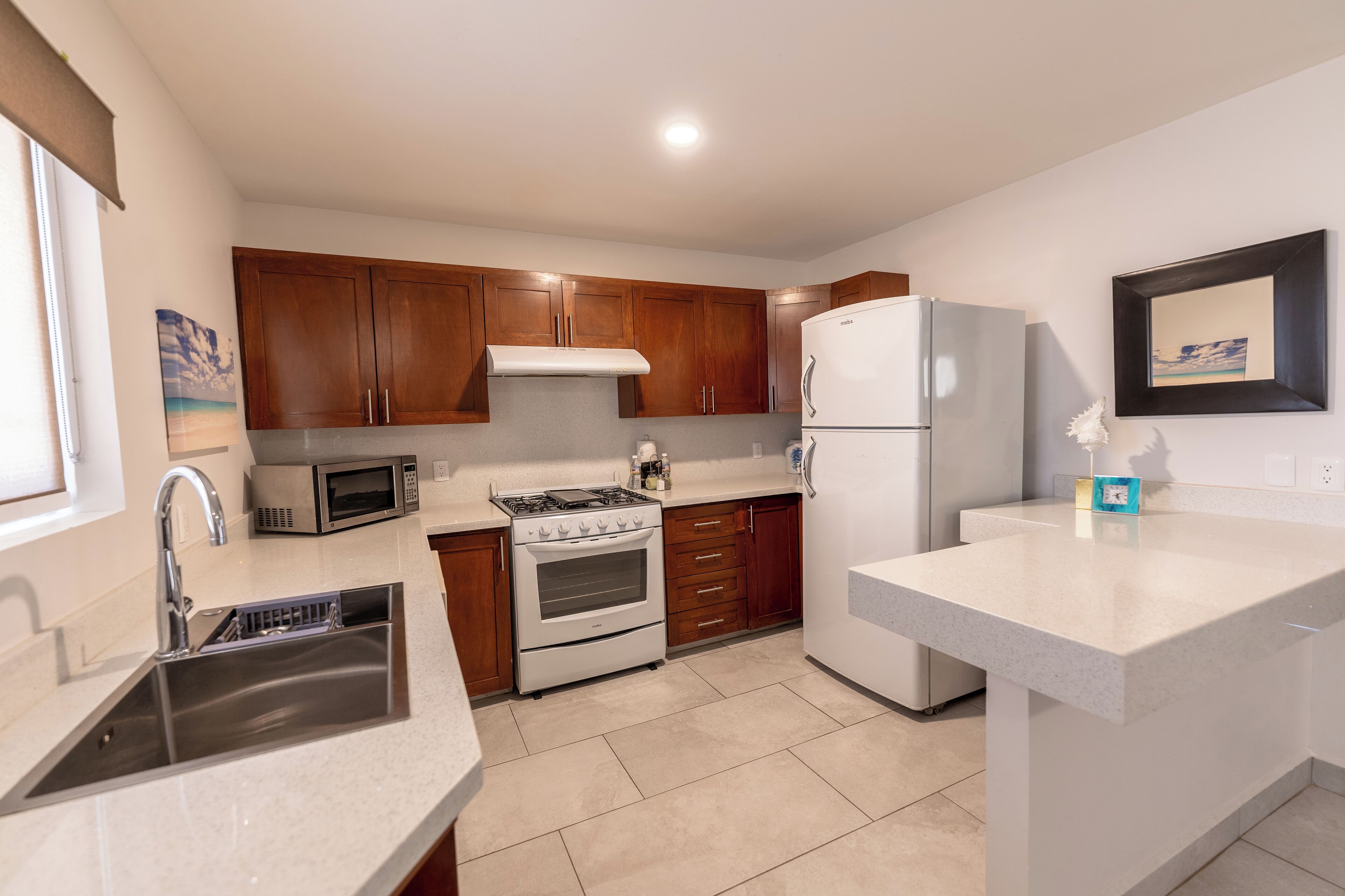 A modern kitchen with wooden cabinets, a stainless steel sink, a microwave, a stove, and a refrigerator.