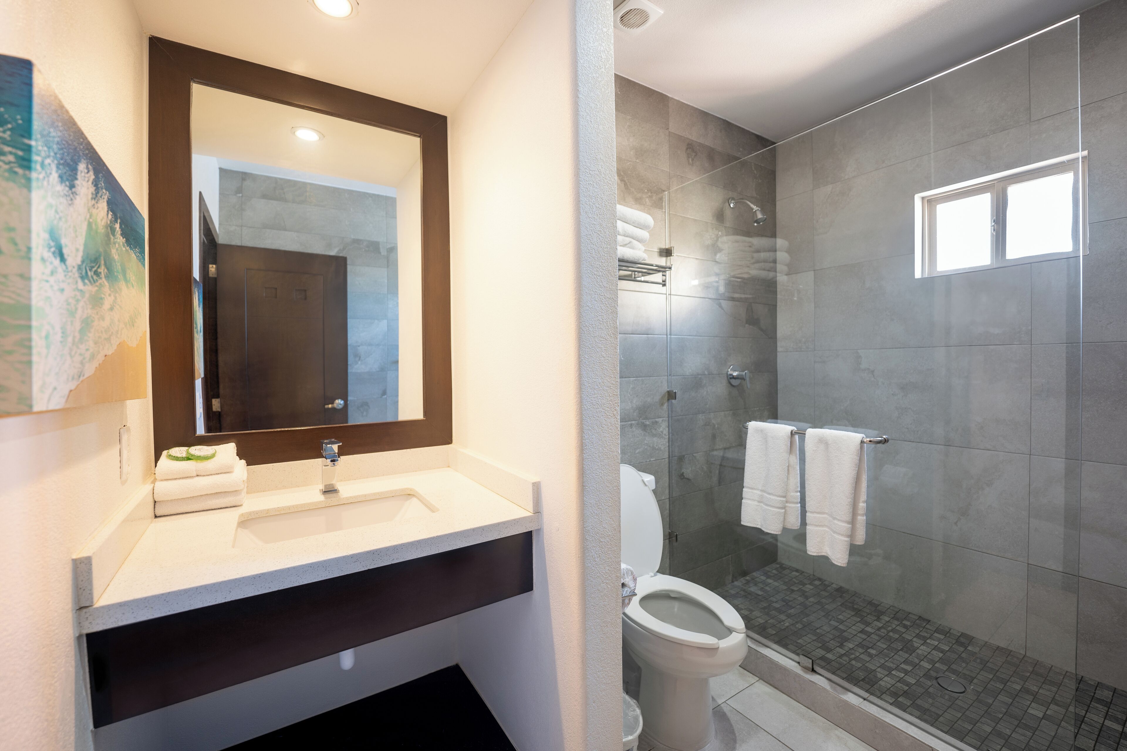 Une salle de bain moderne avec un grand miroir, un lavabo, des toilettes et une douche séparée par une paroi en verre.
