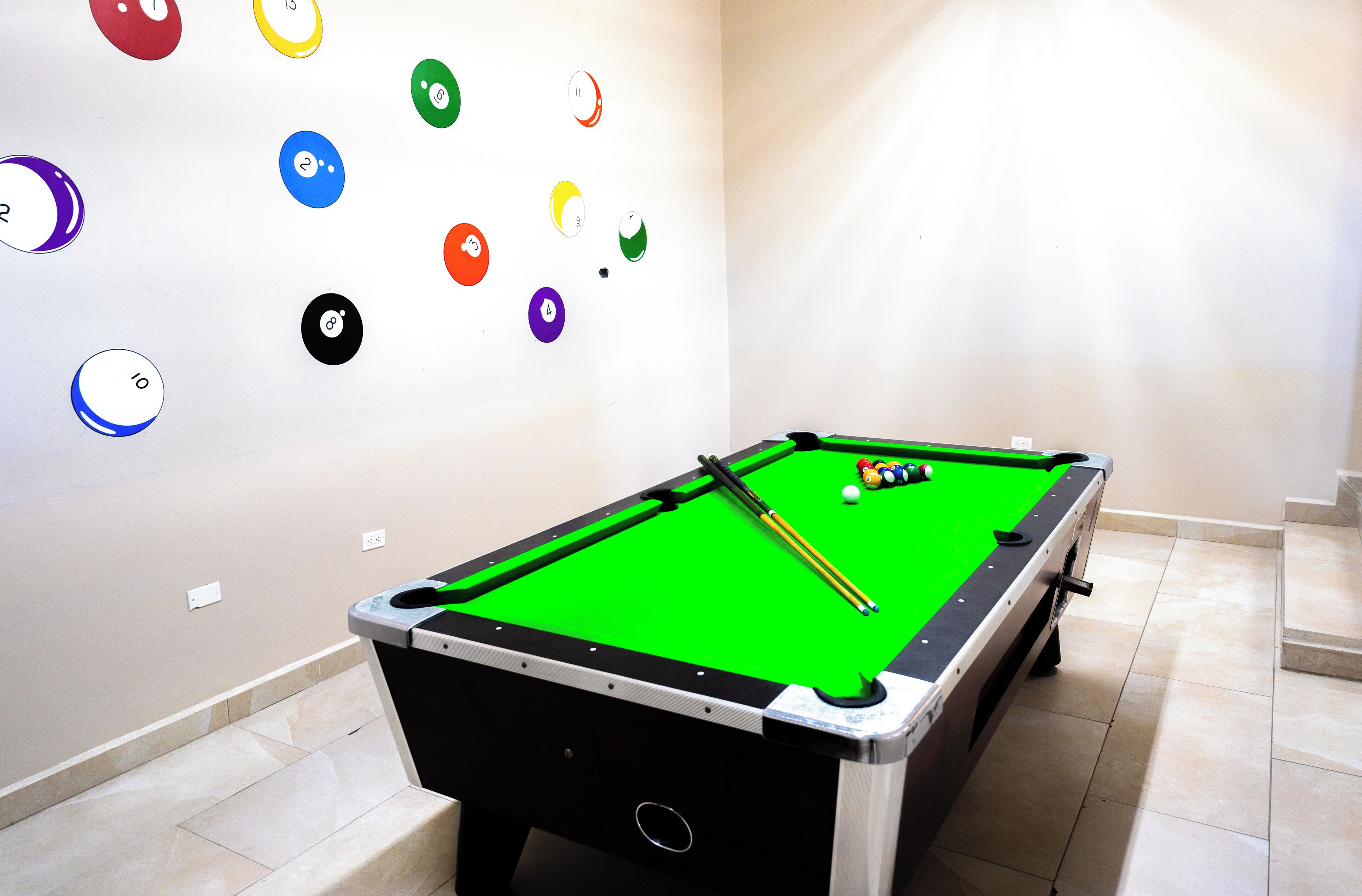 A pool table with a green felt surface, surrounded by a white wall with numbered ball pockets.