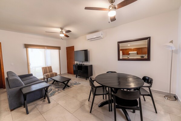 Una sala moderna con sofá, mesa de centro, mesa de comedor con sillas, televisor y ventiladores de techo.