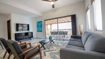 A spacious living room with a ceiling fan, a flat-screen TV, a sofa, a coffee table, and a patterned rug.