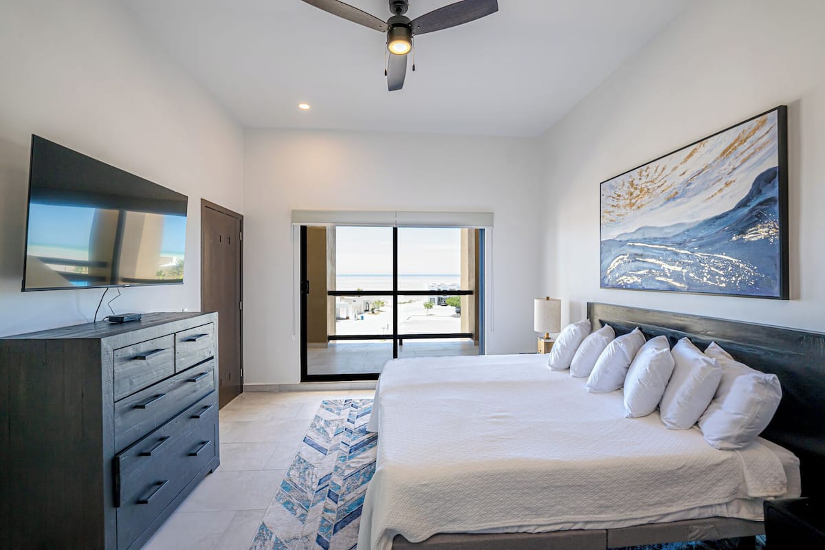 Een moderne slaapkamer met een groot bed, een plafondventilator, een flatscreen televisie en uitzicht door een glazen deur.