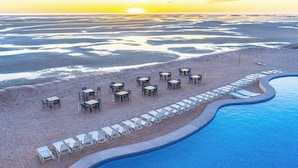 Een zwembad aan het strand met ligbedden en tafels langs de zwemwaterrand.