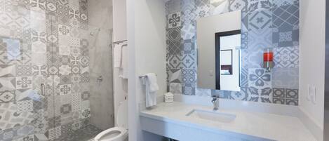 A bathroom with patterned tiles, a glass shower enclosure, a white sink, and a mirror with a red light.