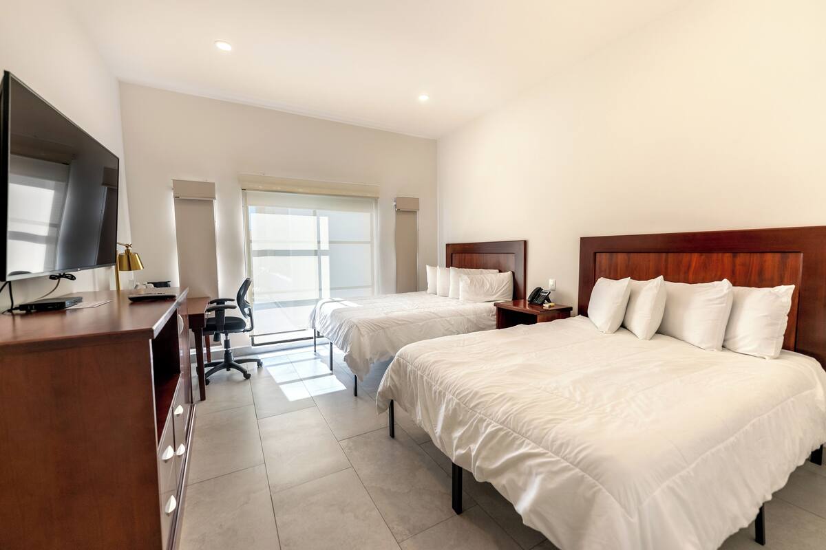 Een hotelkamer met twee bedden, een bureau, een stoel, een televisie en een raam met zonwering.