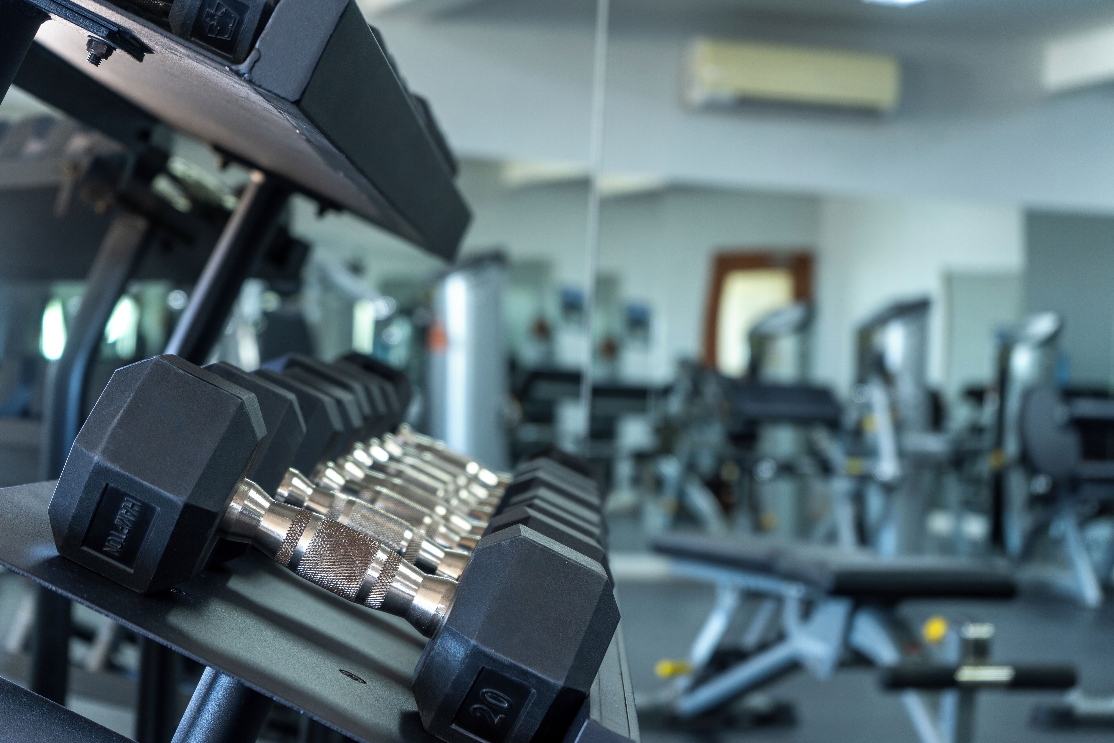 Een sportschool met gewichthefapparatuur, waaronder dumbbells en een bankdrukpers.