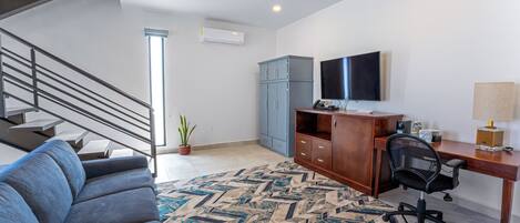 Un salon moderne avec un escalier, un canapé bleu, un bureau en bois, un ordinateur et un téléviseur.