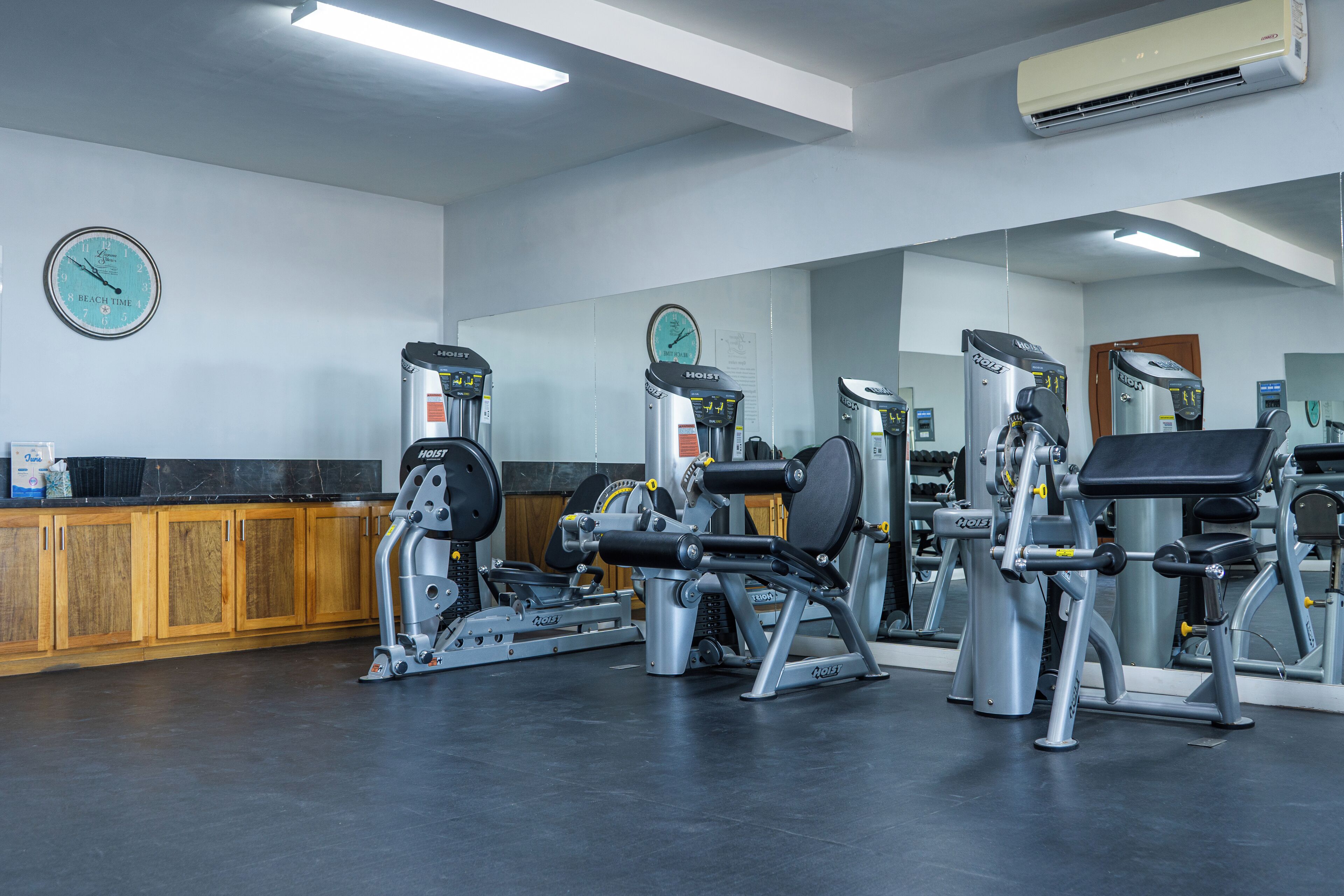 A gym with various exercise machines, wooden cabinets, and a clock on the wall.