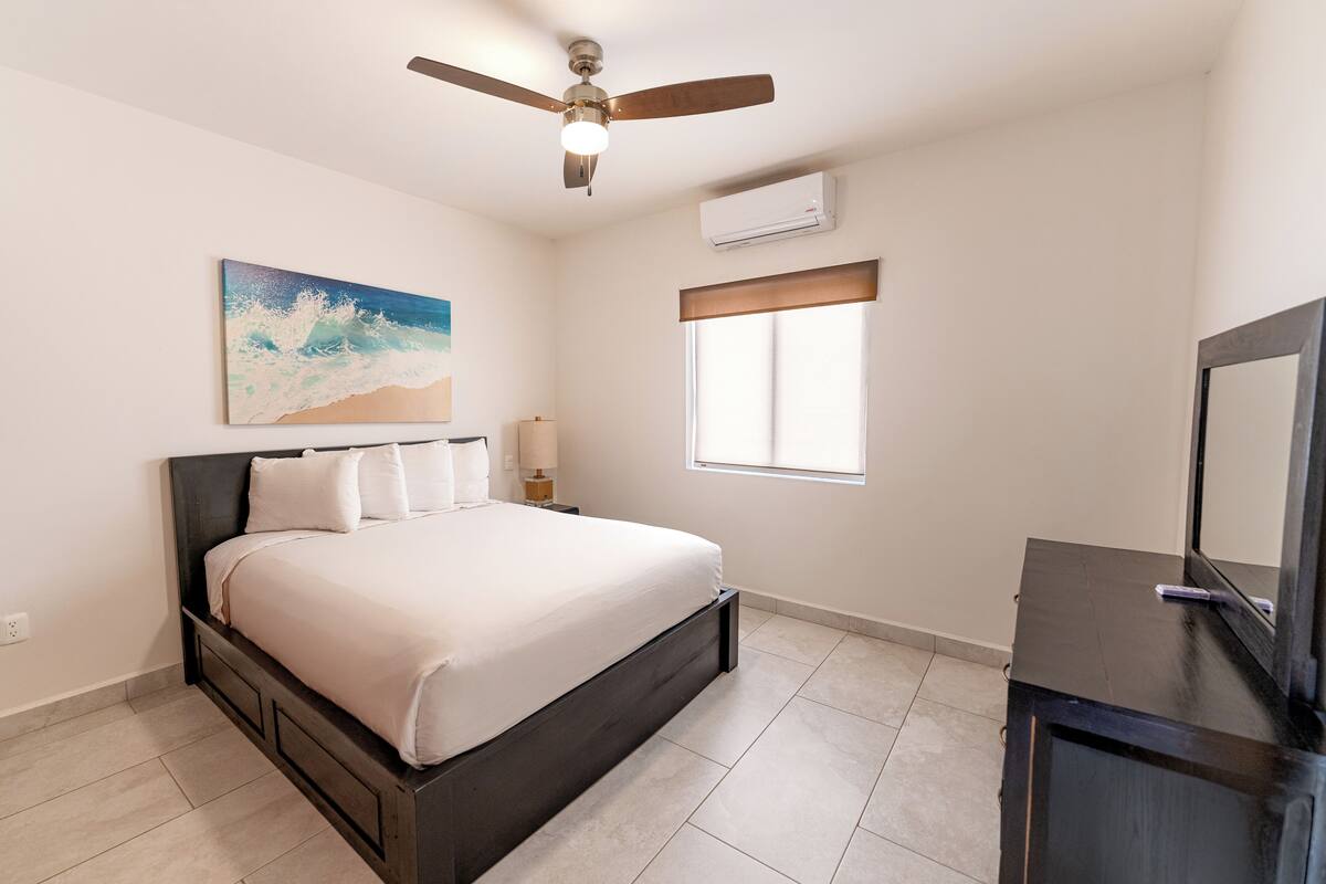 Een slaapkamer met een bed, plafondventilator, airconditioning en een dressoir.