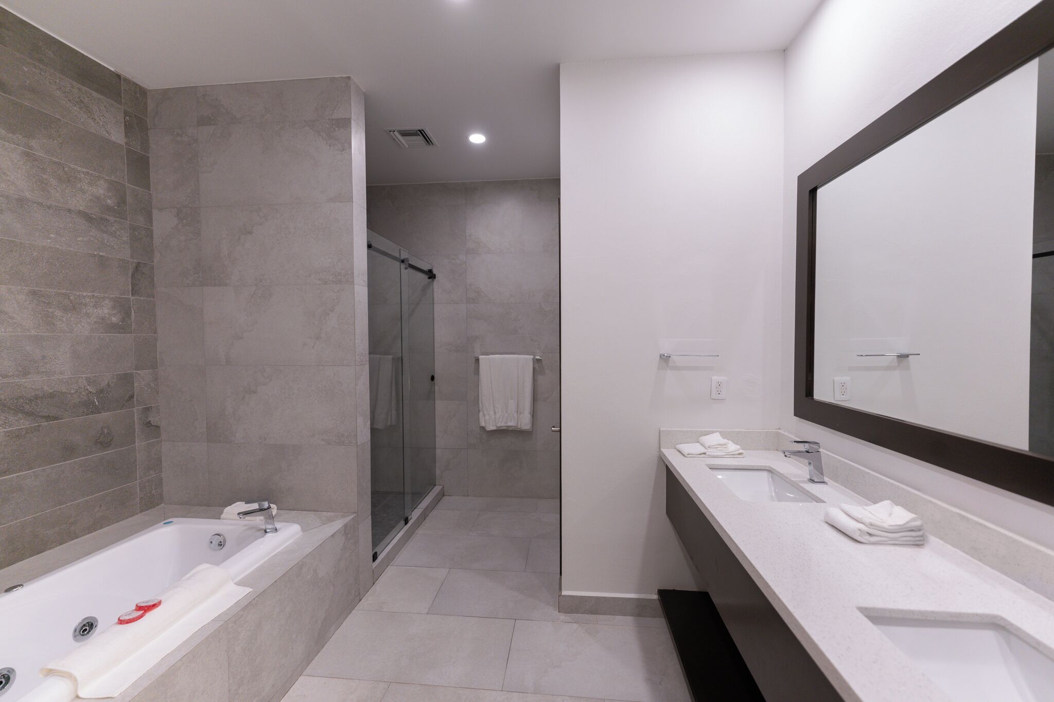 A modern bathroom with a bathtub, a glass-enclosed shower, and a large mirror above the sink.