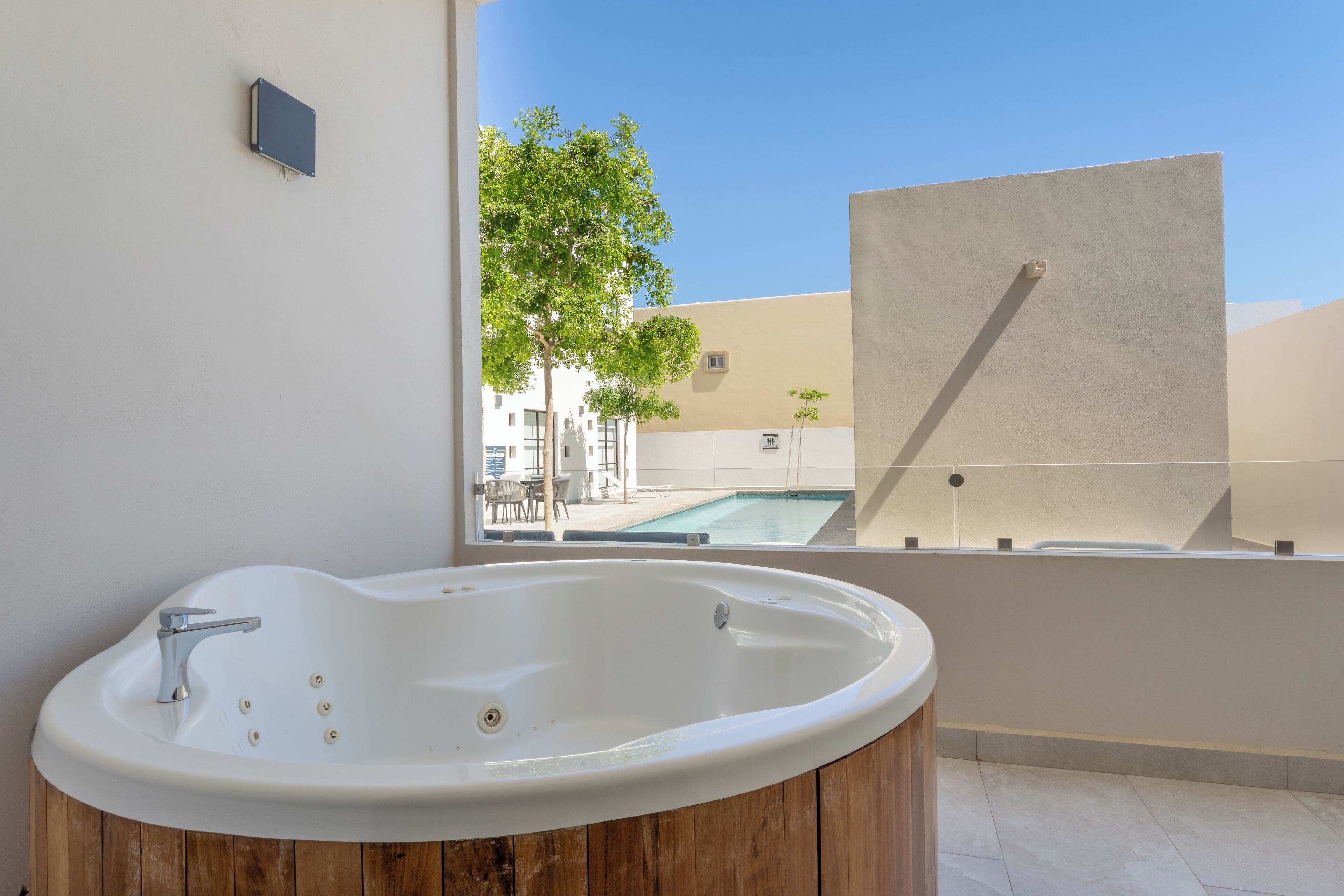 Une salle de bain moderne avec une baignoire îlot, une vue sur une piscine et un meuble-lavabo en bois.