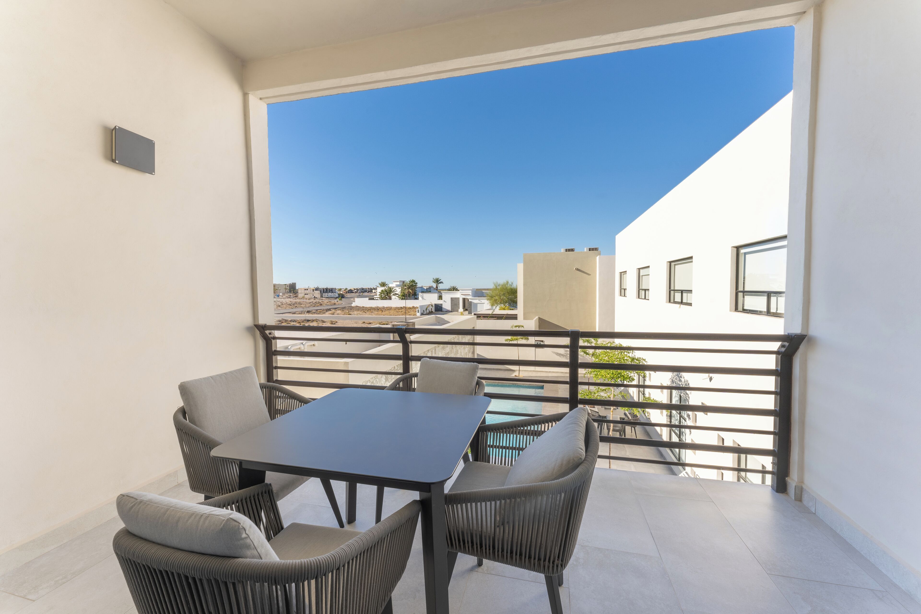 A balcony with a table and chairs, a pool, and a view of buildings and palm trees.