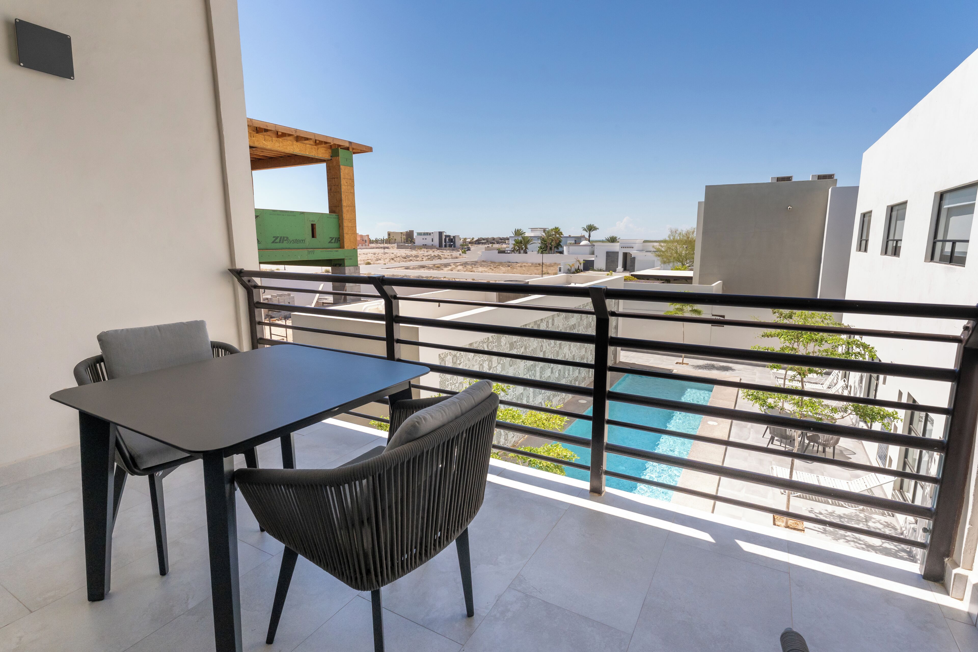 Varanda com mesa e cadeiras, vista para uma piscina e edifícios.