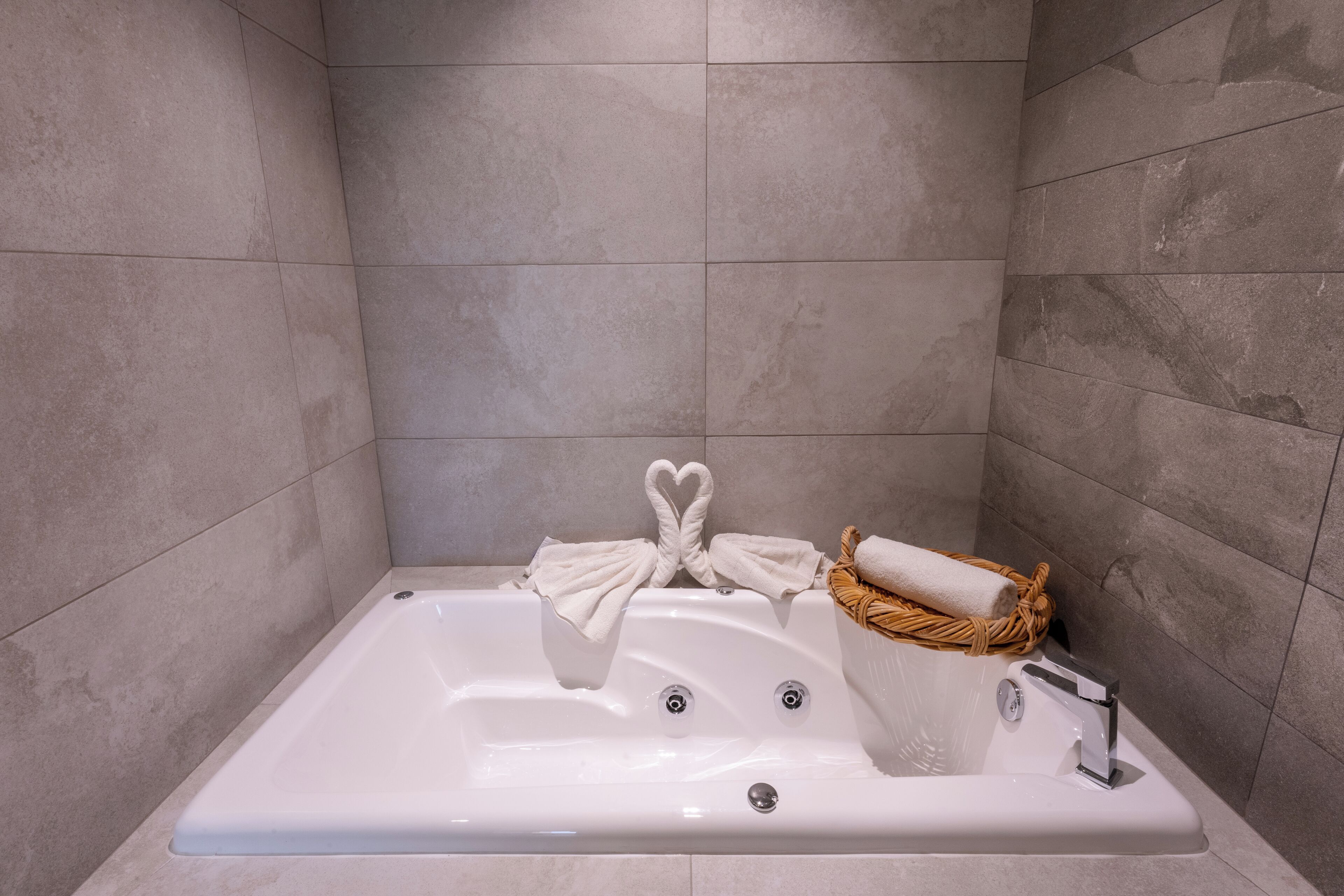 A modern bathroom with a large bathtub, a towel rack with a heart-shaped towel, and a wicker basket with a towel.