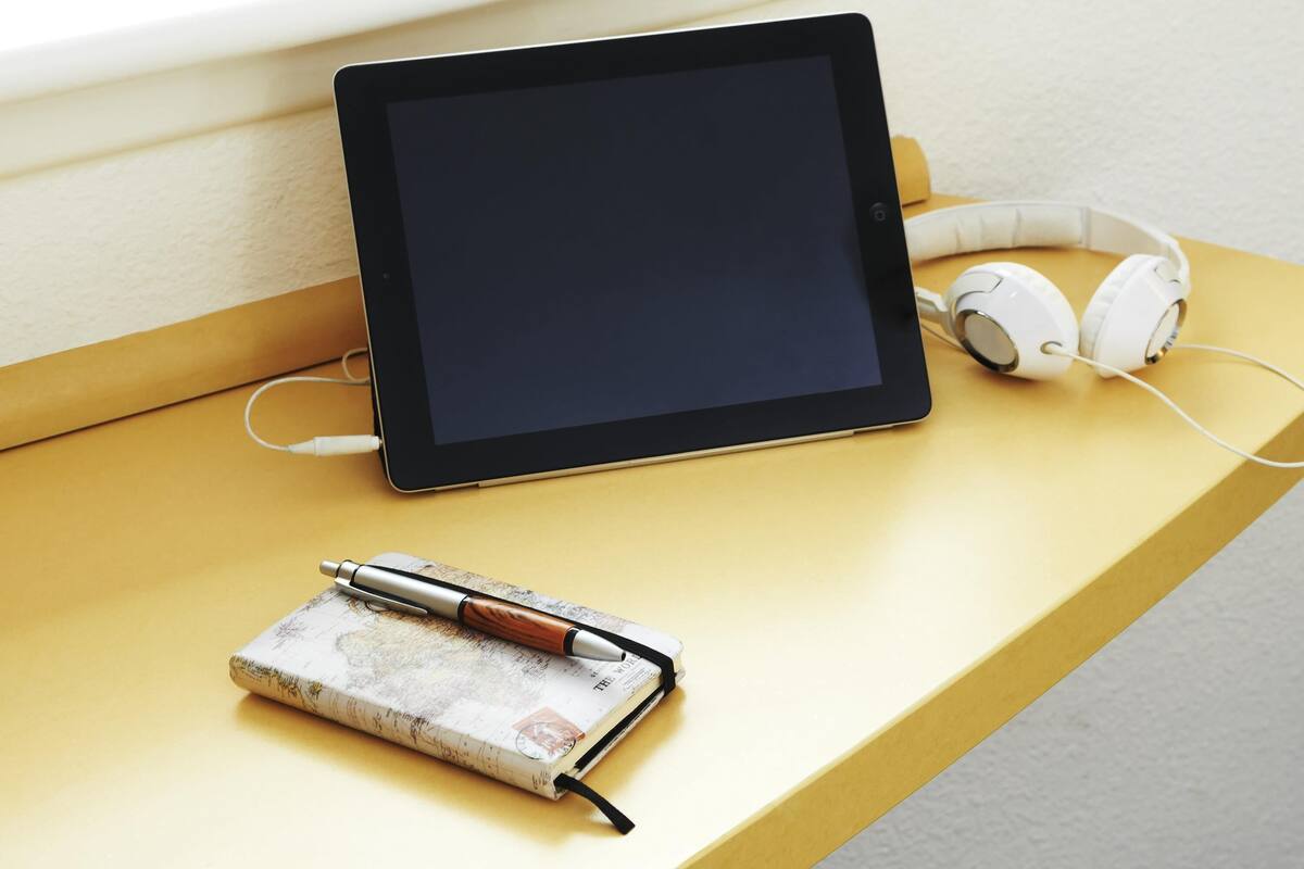 A tablet, headphones, and a pen on a wooden table.
