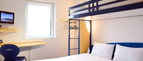 A hotel room with a bunk bed, a desk with a chair, a television, and a window.