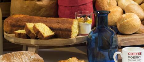 A variety of baked goods including bread, a loaf of cake, and croissants on a wooden board.