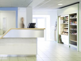 A reception area with a counter, a bookshelf with various items, and a staircase leading to another level.