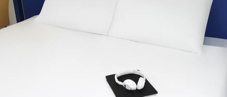 Un lit avec une literie blanche, un oreiller noir et des écouteurs blancs posés sur une taie d’oreiller noire.
