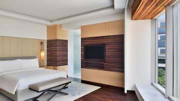 A modern hotel room with a large bed, a bench, a flat-screen TV mounted on the wall, and a large window offering a view of the city.