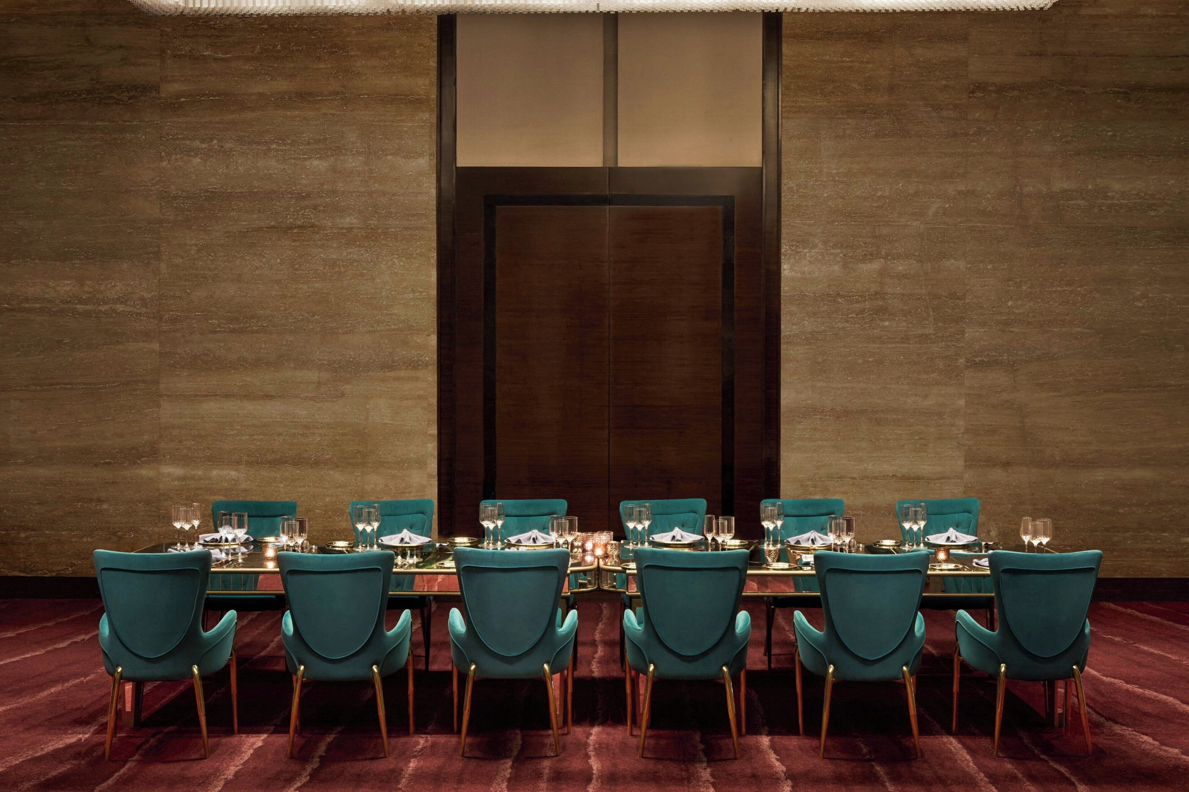 Une salle de conférence avec une longue table, des chaises de couleur turquoise et une porte en bois foncé.