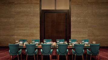 Une salle de conférence avec une longue table, des chaises de couleur turquoise et une porte en bois foncé.