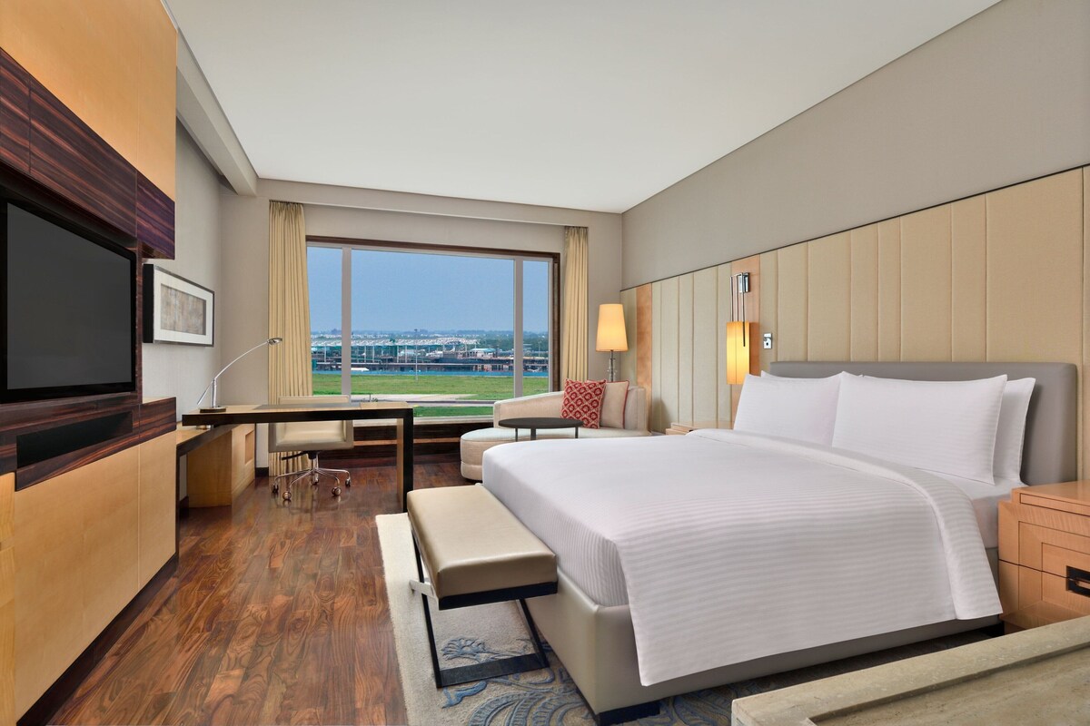 Habitación de hotel con una cama grande, un escritorio, una silla, un televisor y vistas a la ciudad.