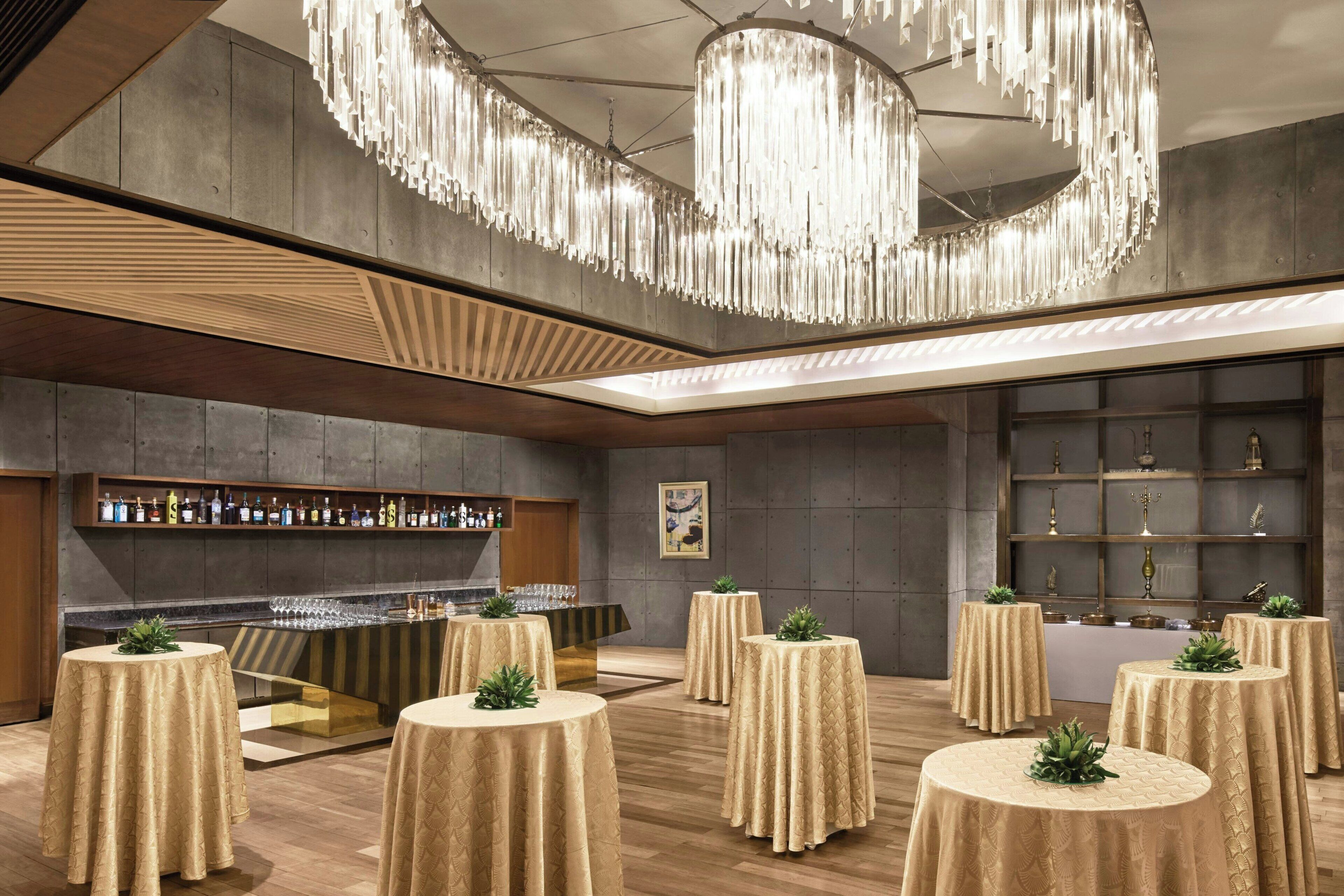 A modern bar area with round tables, a bar counter, and a decorative chandelier.
