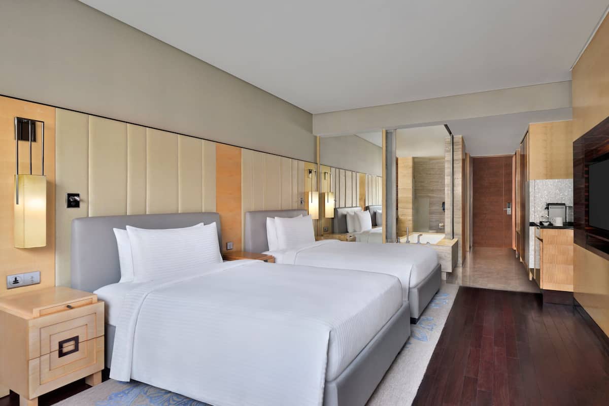 A hotel room with two beds, a wooden floor, a bathroom with a bathtub, and a TV.