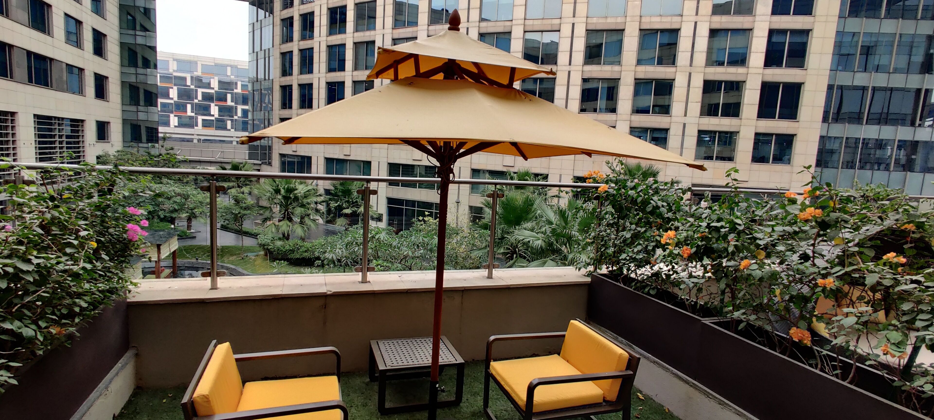 Un balcón con dos sillas amarillas acolchadas, una mesa y un parasol beige.