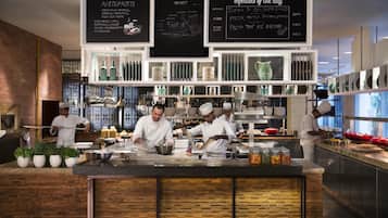 Una cocina moderna con chefs preparando alimentos, un menú en pizarra y utensilios de cocina ordenados.