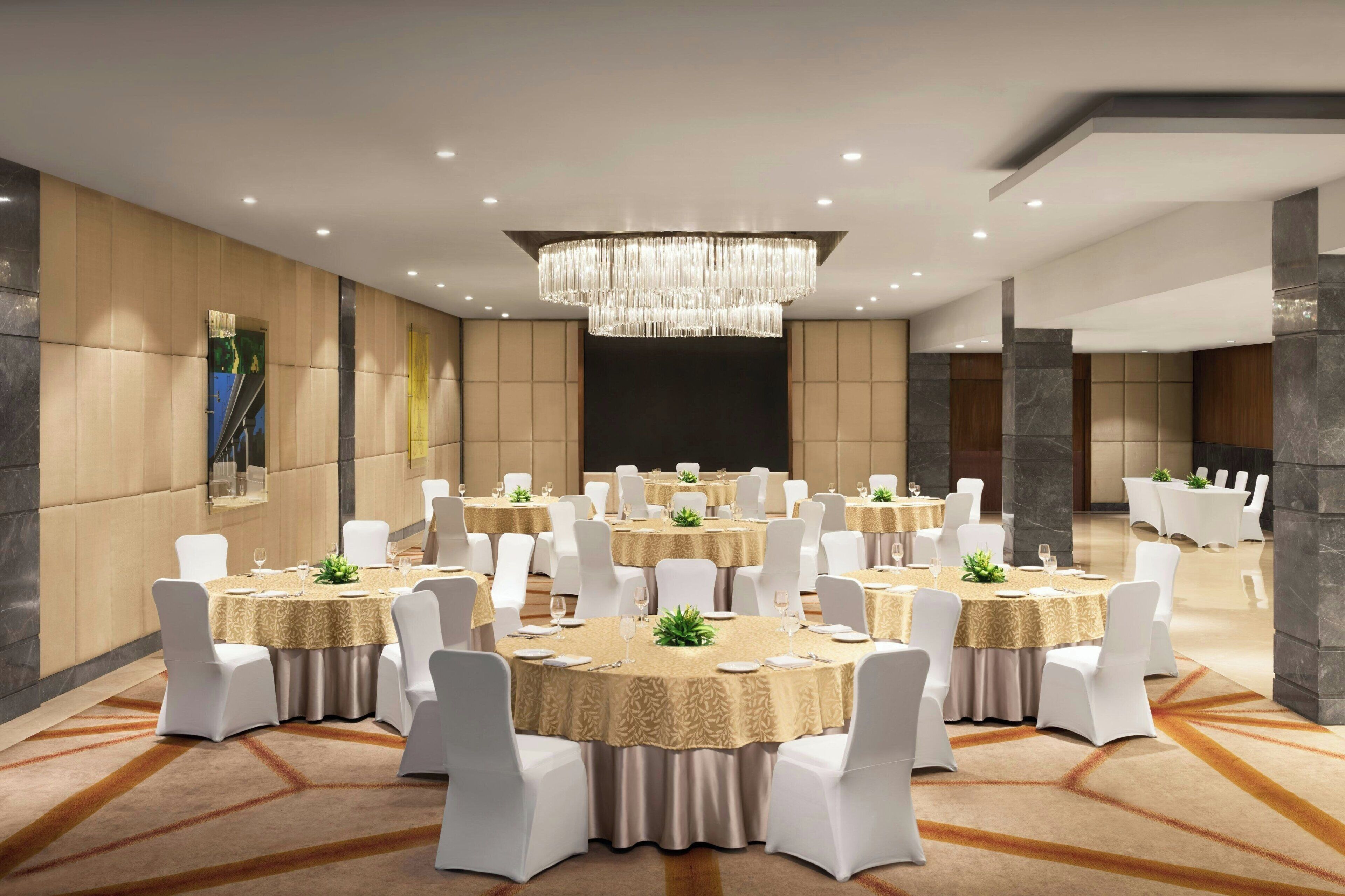 A conference room with multiple tables, white chairs, and a chandelier.