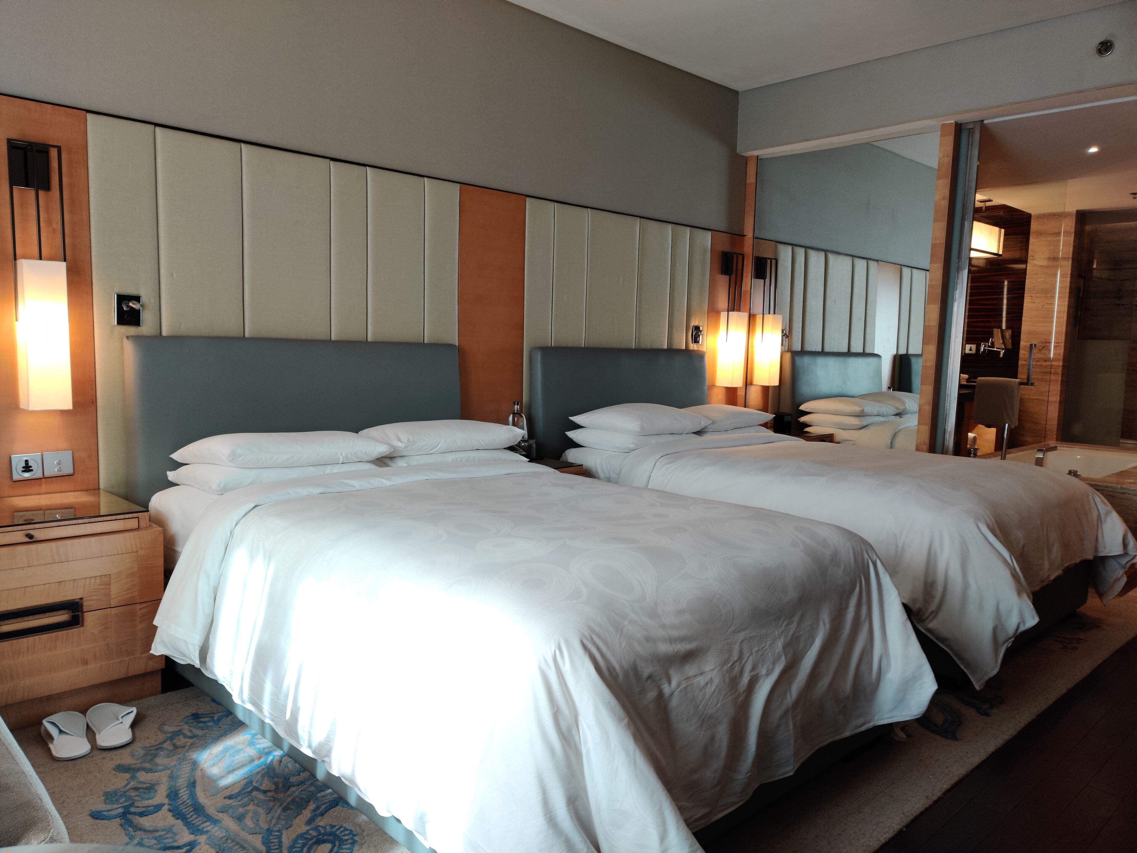 Une chambre d’hôtel avec deux lits, un grand miroir et une salle de bain avec baignoire.