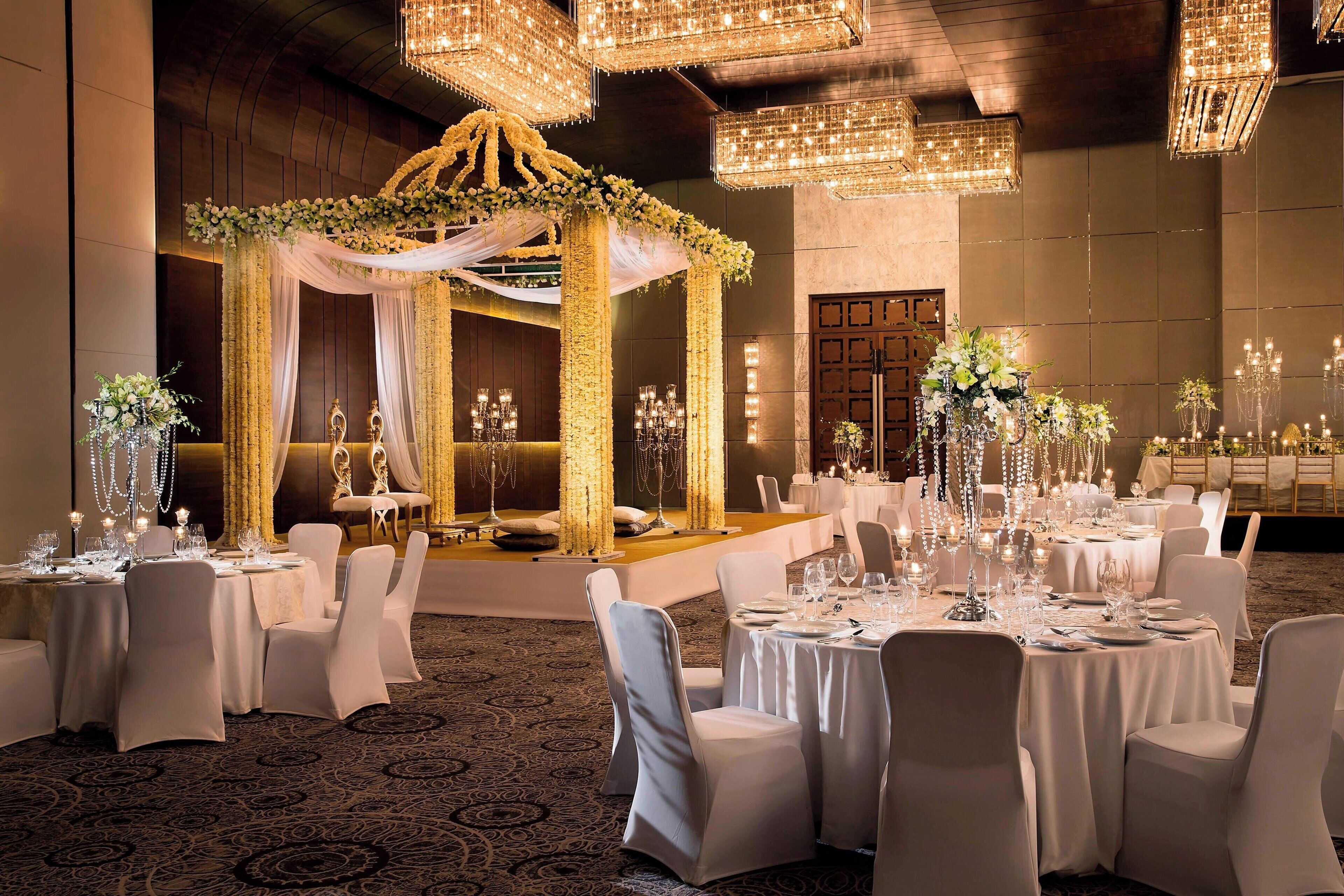 A banquet hall with round tables, white chairs, and chandeliers.
