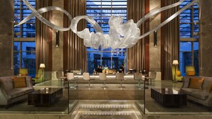 A modern lobby with a glass coffee table, seating area, and a large decorative sculpture.