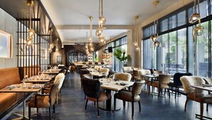 A modern restaurant with high ceilings, hanging pendant lights, and a mix of booth and table seating.
