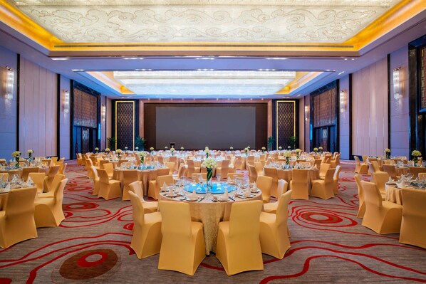 Un salón de banquetes con mesas redondas, sillas amarillas y una pantalla grande al frente.
