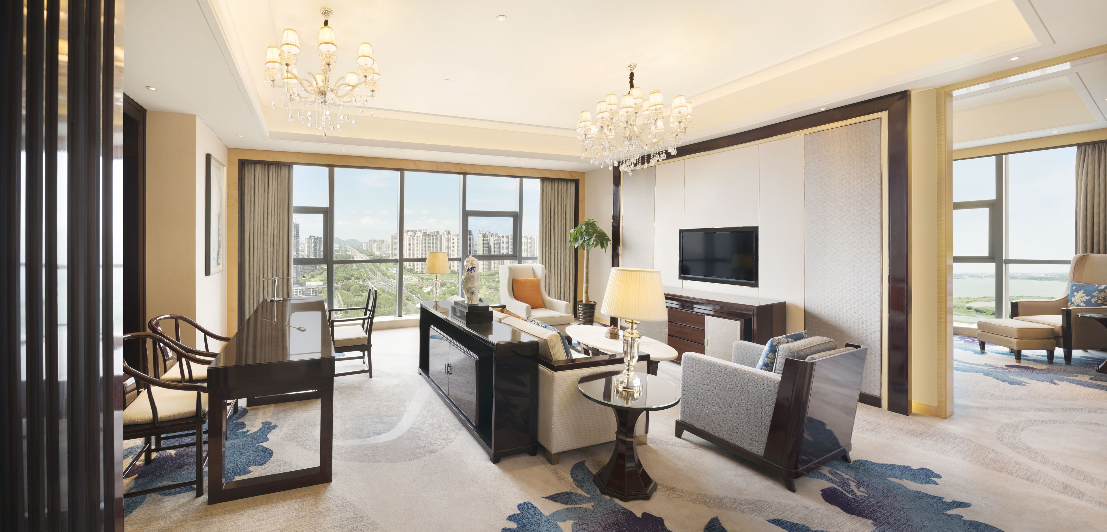 Un hotel moderno con una ventana grande que ofrece vistas a la ciudad, un área de comedor con una mesa y sillas, un sofá, un televisor y una araña.