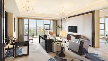 Un hotel moderno con una ventana grande que ofrece vistas a la ciudad, un área de comedor con una mesa y sillas, un sofá, un televisor y una araña.