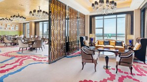 Un vestíbulo amplio con techo alto, candelabros, una zona de estar con sofás y sillones, un separador decorativo y ventanas grandes que ofrecen vistas.