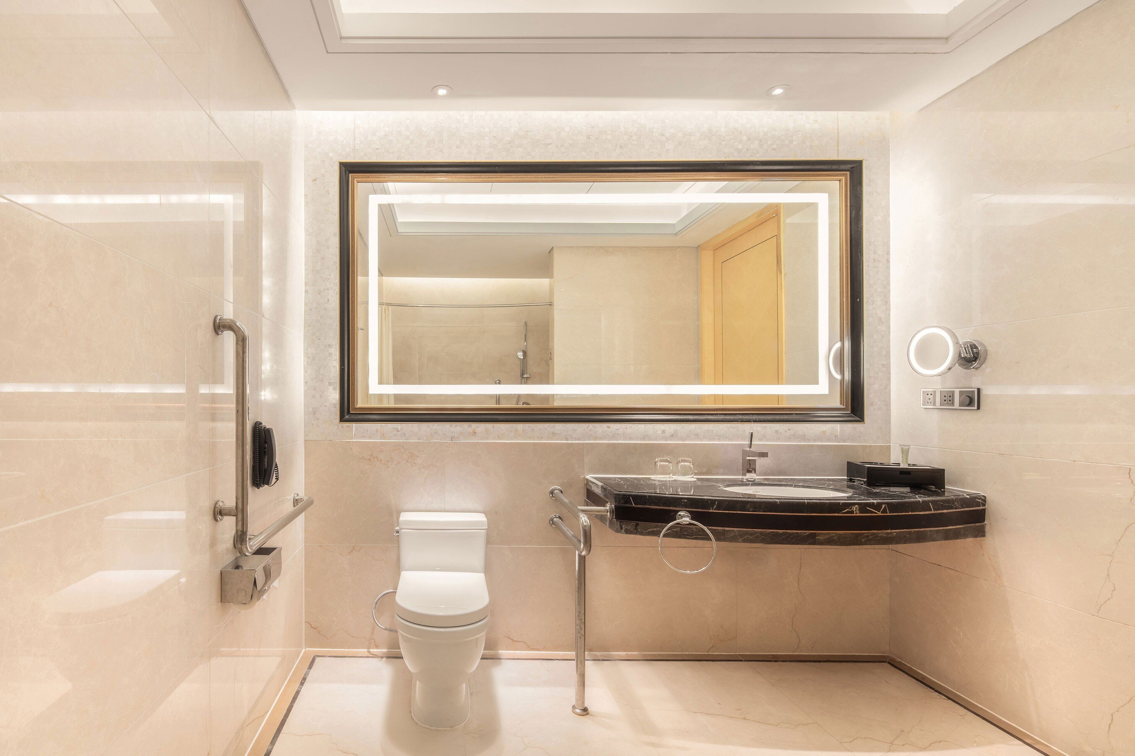 Et moderne badeværelse med et stort spejl, toilet, vask med marmorbordplade og bruseområde.