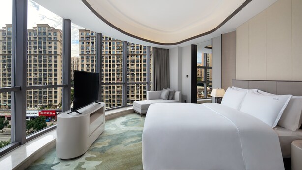 A modern hotel room with a large bed, a TV, and a view of high-rise buildings. - Holiday Inn Ningde Xiapu by IHG (Ningde)