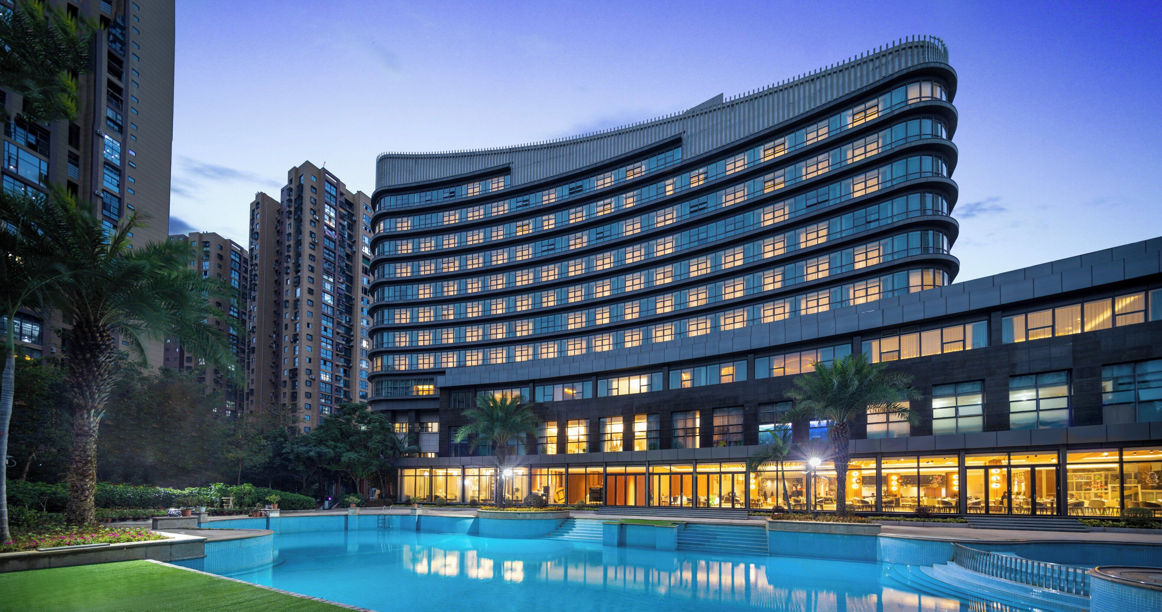 Un hôtel moderne à la façade incurvée, doté de plusieurs étages et d’une piscine située en premier plan.