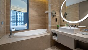 A modern bathroom with a large bathtub, a round mirror with a light, and a window offering a view of a building. - Holiday Inn Ningde Xiapu by IHG (Ningde)