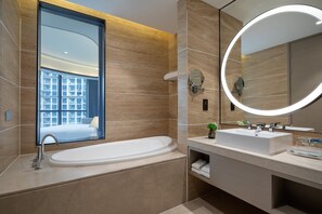 A modern bathroom with a large bathtub, a round mirror with a light, and a window offering a view of a building. - Holiday Inn Ningde Xiapu by IHG (Ningde)
