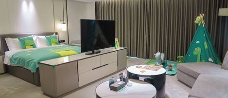 Moderni hotellihuone, jossa on sänky, televisio, sohva, sohvapöytä ja pieni leikkiteltta.