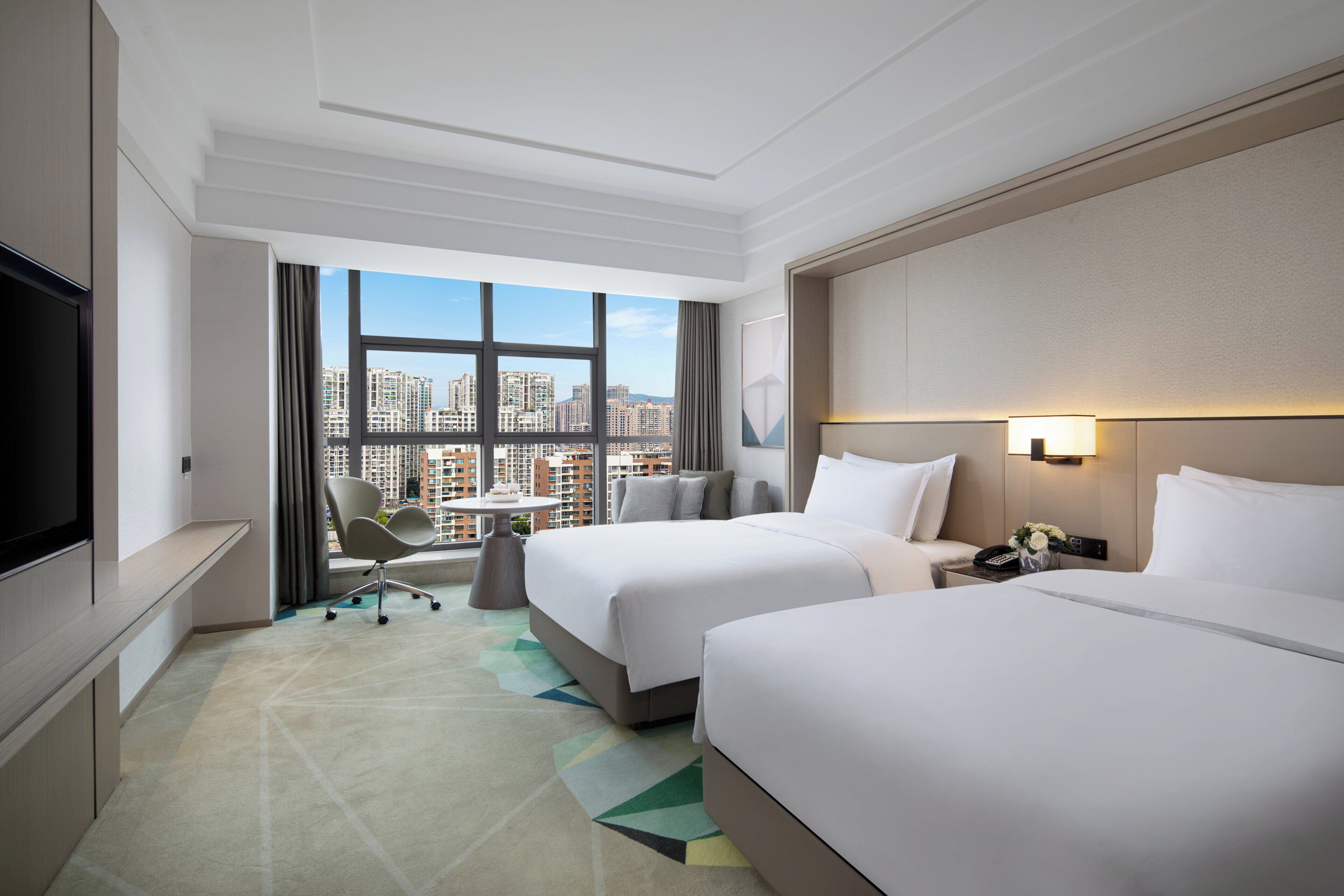 Une chambre d’hôtel avec deux lits, une télévision, un bureau et une vue sur la ville.
